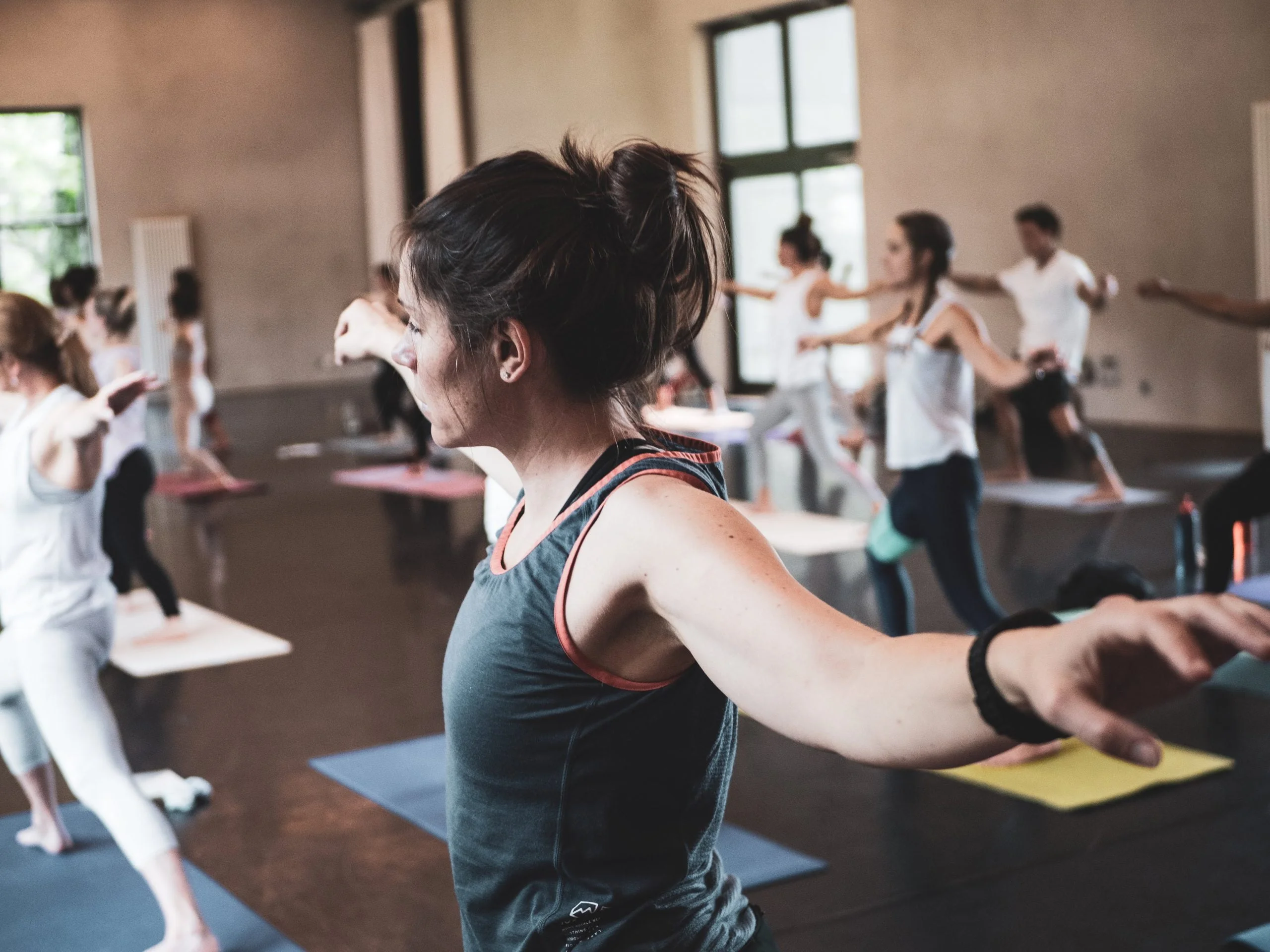 Gros plan sur une jeune femme en posture du guerrier 2, entourée d'autres femmes pratiquant un exercice de compréhension des principes du Strala Yoga