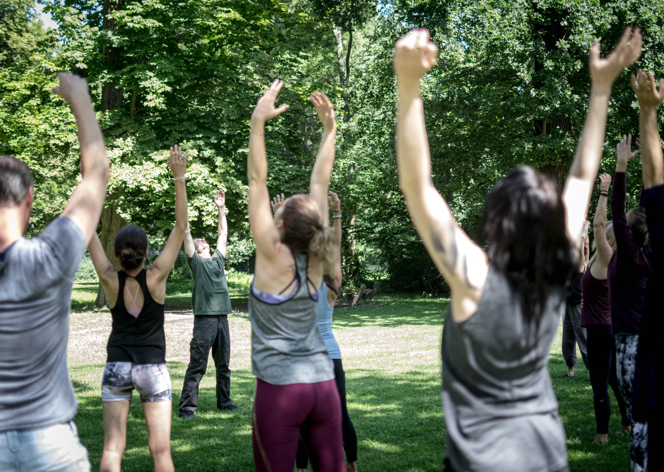 Des jeunes femmes debout dans un parc, les bras en l'air, guidées par Mike Taylor, fondateur du Strala Yoga, dans une démonstration des principes du Strala Yoga