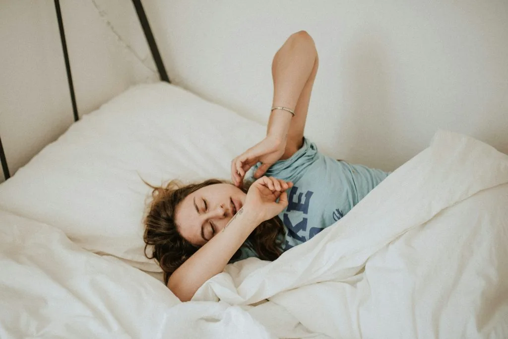 Jeune femme dans son lit en train de se réveiller, peut-être fatiguée