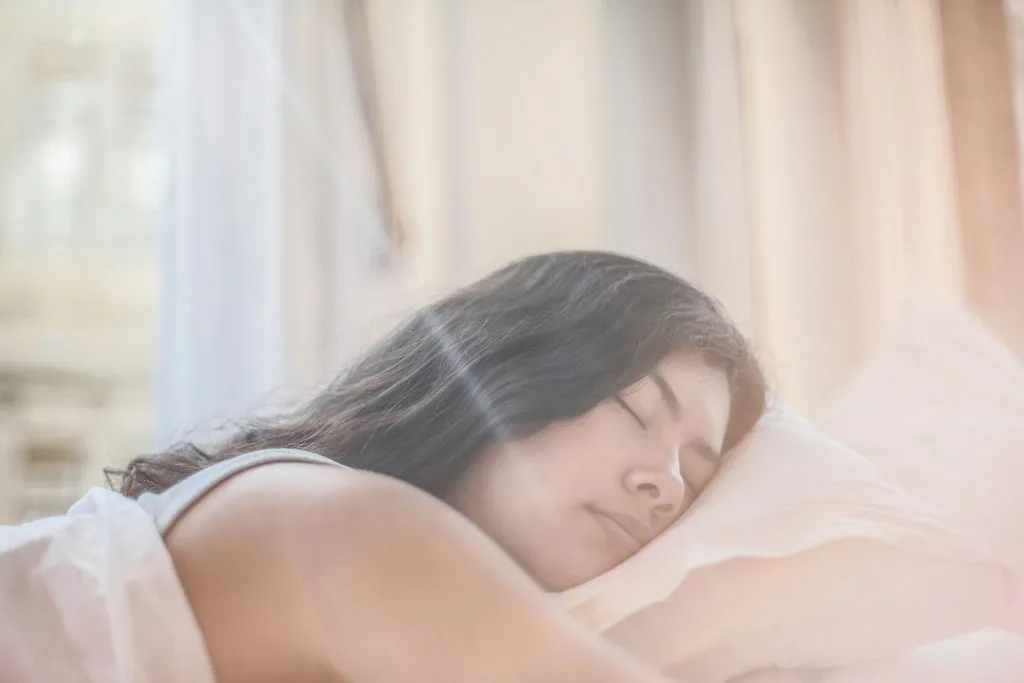 Jeune femme dans son lit les yeux fermés, détendue après une séance de yoga pour dormir