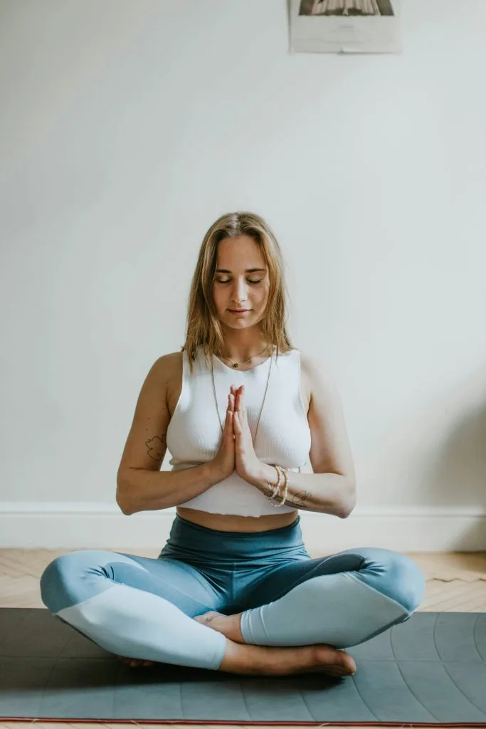 Jeune femme assise en tailleur sur son tapis, les mains en prière au niveau du coeur, en train de pratiquer le Yoga Nidra