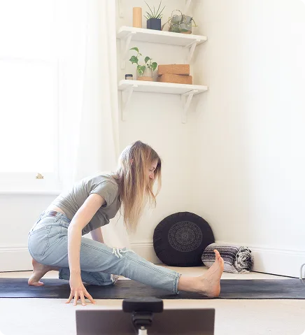 Une professeur de yoga en posture du demi grand écart sur un tapis donne un cours en direct sur Zoom