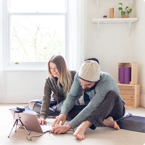 Deux professeurs de yoga, assis sur un tapis, qui se préparent pour un cours de yoga en direct sur Zoom