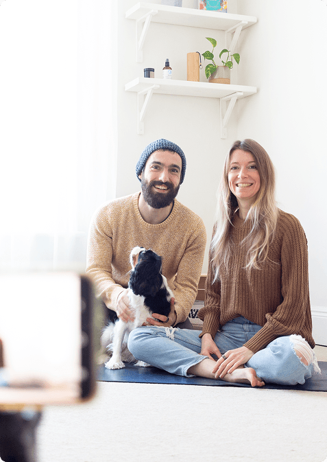 Un couple avec un chien assis sur un tapis de yoga face à une caméra
