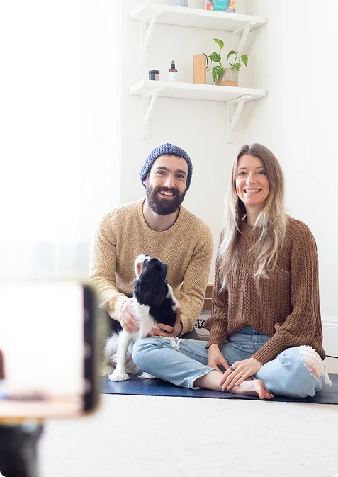 Un couple avec un chien assis sur un tapis de yoga face à une caméra